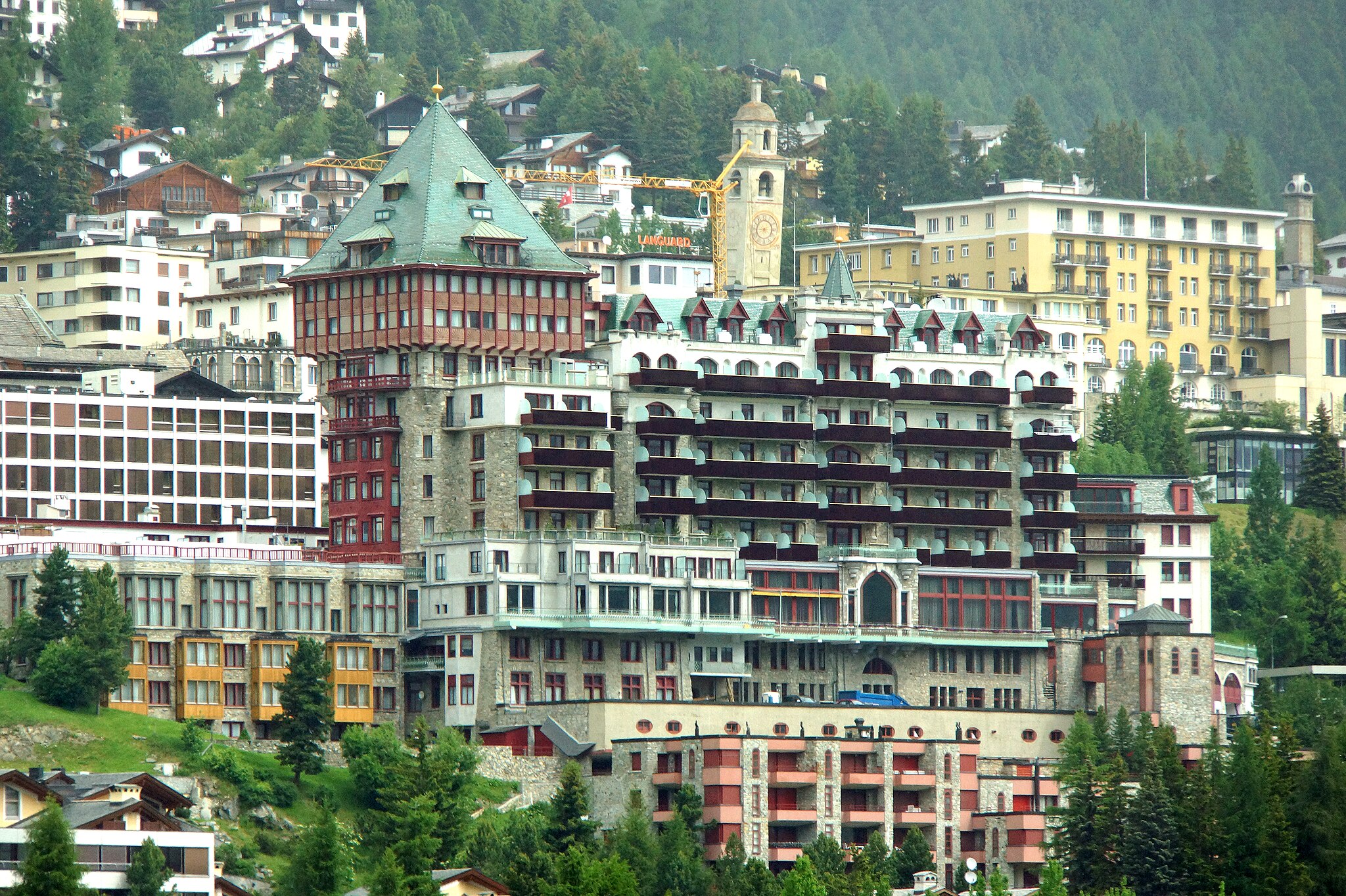 A lavish ski resort building amidst other high-end buildings on a mountainside covered with pines.