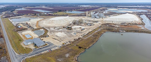 Aerial view of a plant mining sand for fracking. The view shows a constellation of quarries, industrial plants and other infrastructure, and holding ponds. The background shows what looks like a solar panel farm.