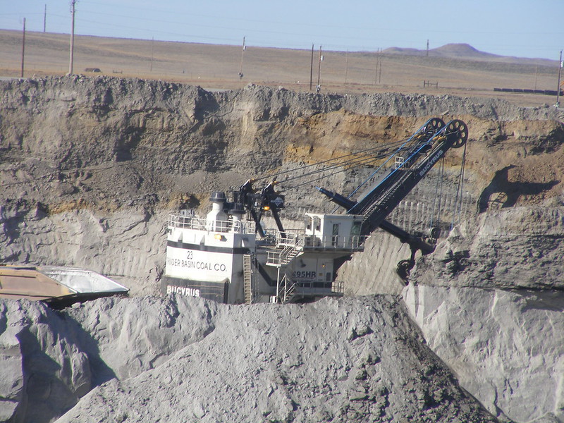 Machinery digging in a giant pit in a flat, desertous landscape.