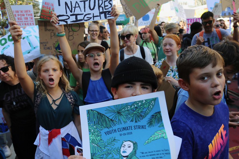 A crowd of children holding signs with environmental slogans, with their mouths open, shouting or singing.
