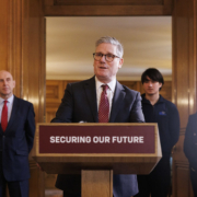 54363122568_e6cb196daa_c Starmer stands at a podium with four people (including two young people) standing behind him.