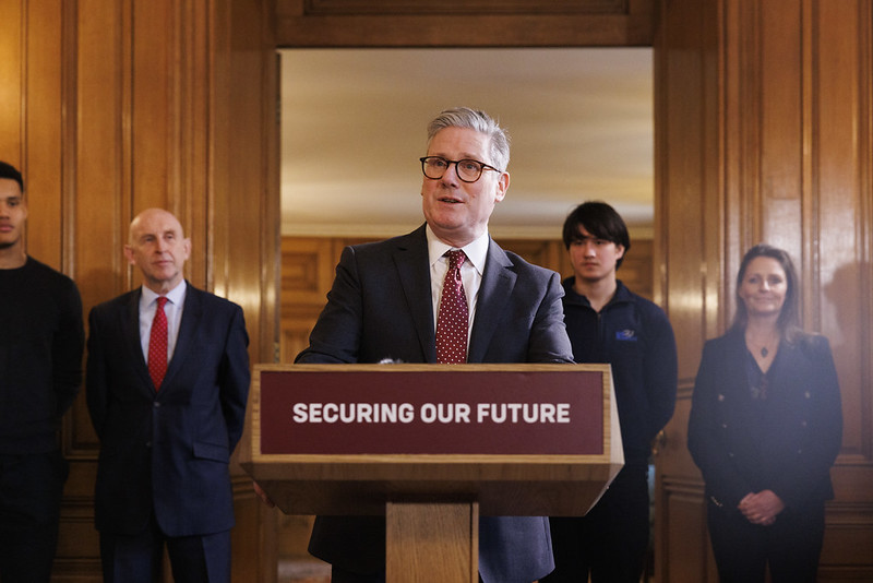Starmer stands at a podium with four people (including two young people) standing behind him.