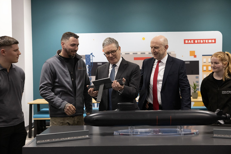Starmer looks down at a gadget in his hands with four smiling people standing around him, two of them youth.