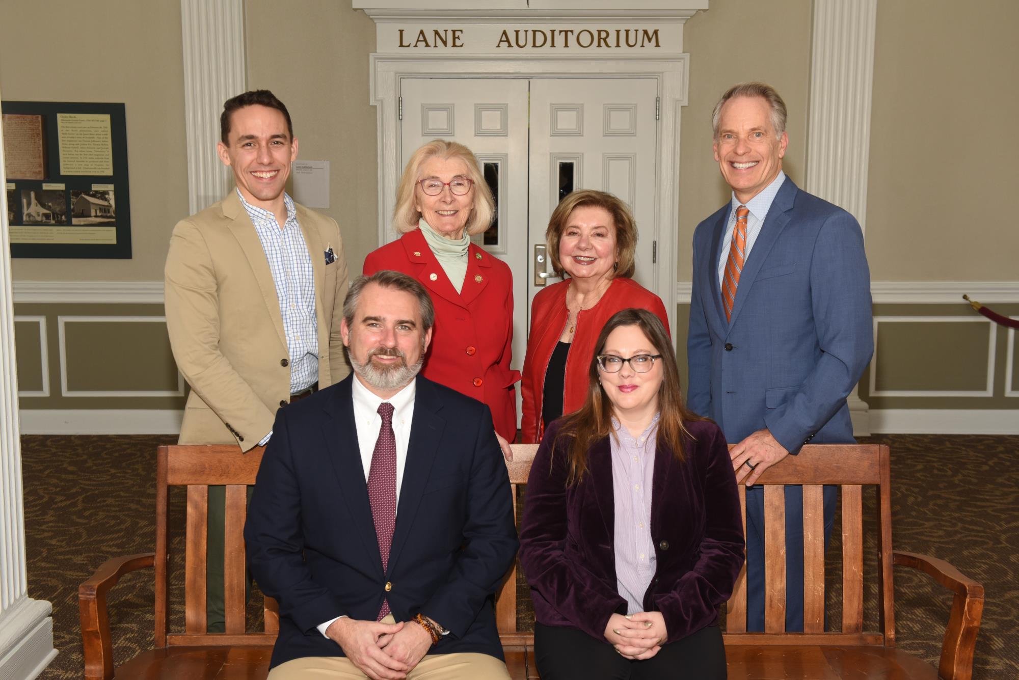 6 people in business attire pose and smile inside an official-looking building.