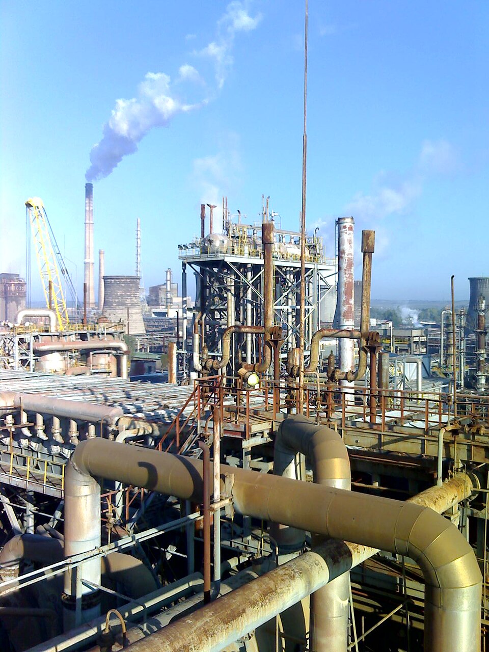 A labyrinth of metal infrastructure with smoke rising from smokestacks in the background.
