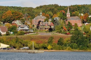 photo from the water looking toward the shoreline of Bayfield, Wisconsin. Buildings surrounded by autumn colors are seen
