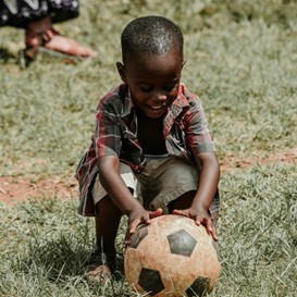 young African boy playing with a soccer ball in a field