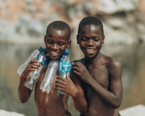 two boys holding four plastic water bottles