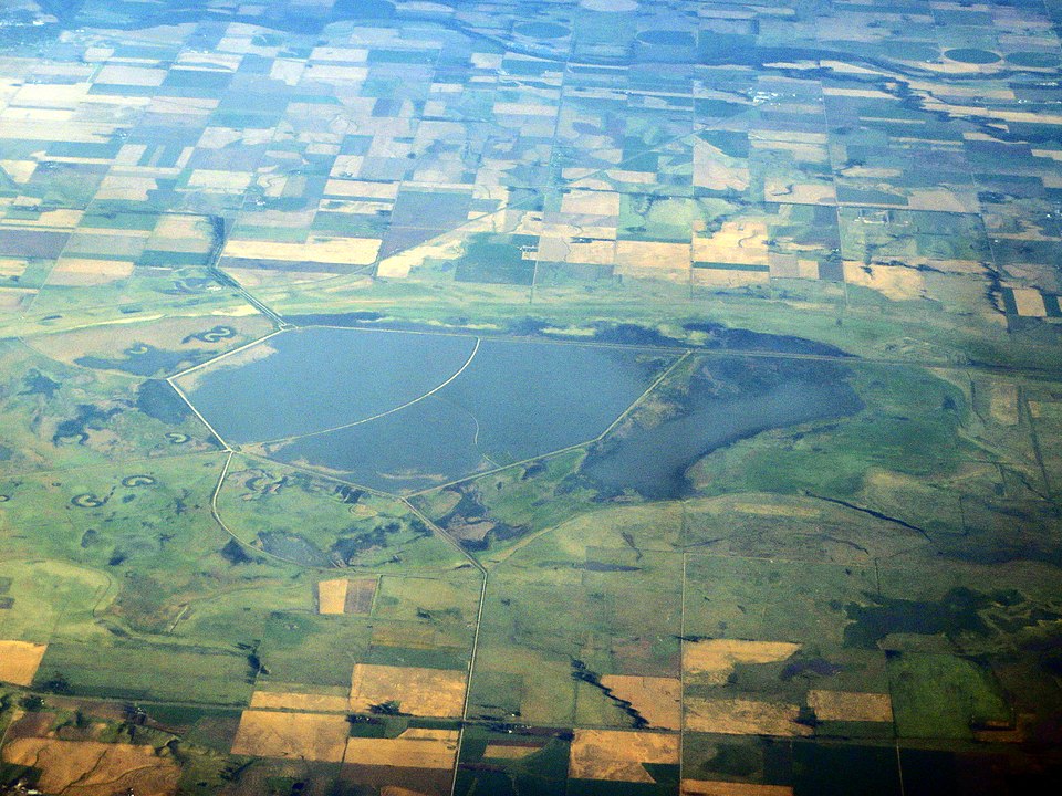 A wetland surrounded by green, yellow, and brown agricultural fields.