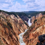 Vast canyon with a white river running through it and green mountains in the distance.