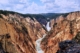 Vast canyon with a white river running through it and green mountains in the distance.