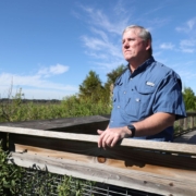 Hoctor stands on boardwalk overlooking wide-open, vegetated space.