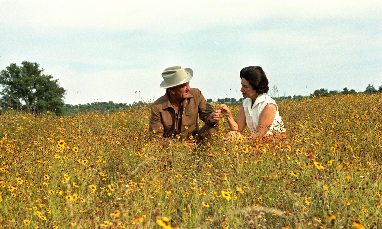 President Johnson and Lady Bird Johnson sit in a field of daisies, their hands touching