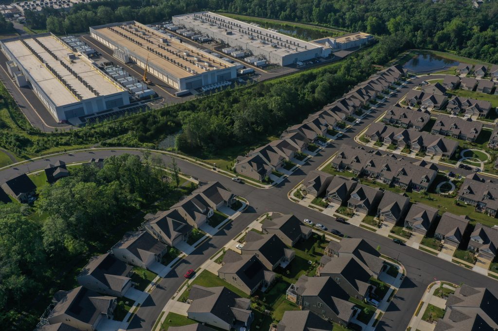 A giant data-center complex separated by a thin line of trees from a housing division.