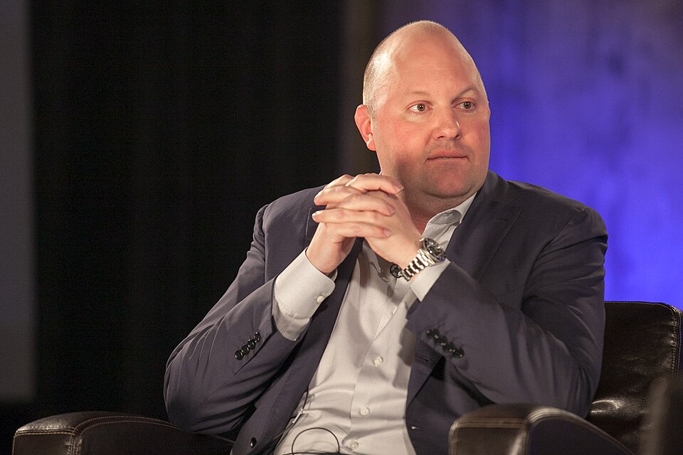 Andreessen sits on an armchair with his hands clasped, wearing a suit and a serious face.