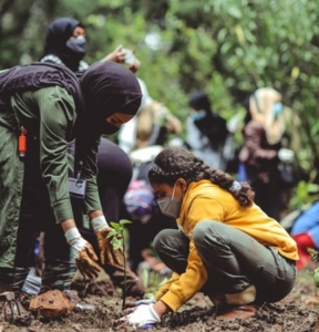 Two girls, one wearing a hijab, planting a tree
