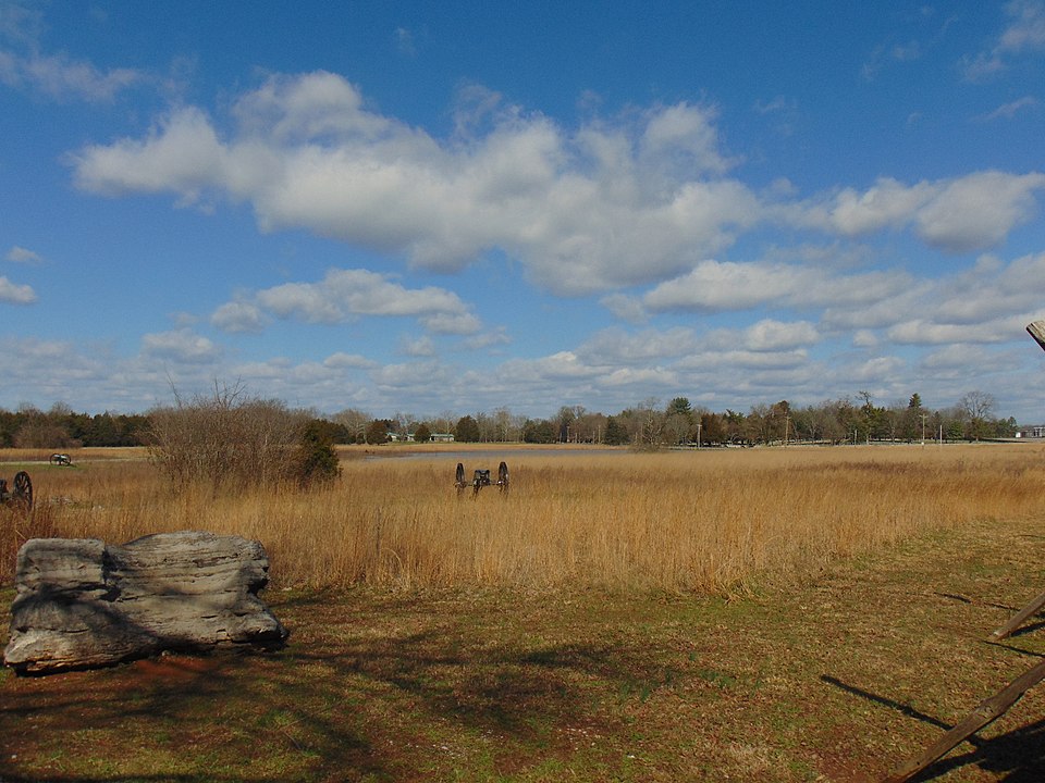 An old cannon sits in a field of yellow grass with blue sky and clouds.