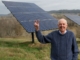 Wendell Berry standing next to solar panels and displaying the peace sign