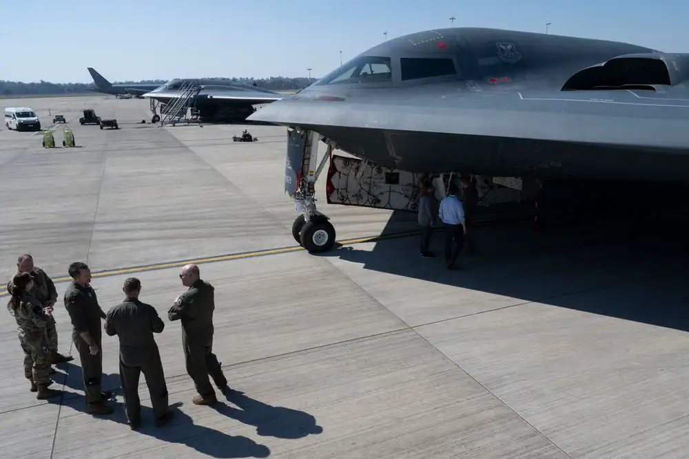 A group of military personnel stand near black, sleek aircraft.