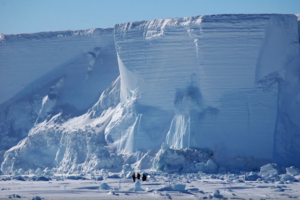 image of very high ice cliffs towering over people walking below