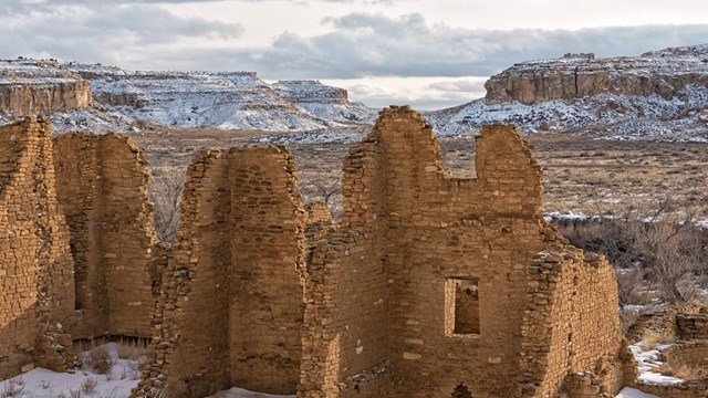 clay brick ruins in the foreground with sprawling, snow-covered canyons in the background