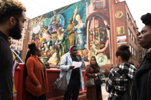 speaker and listeners in front of a giant mural.