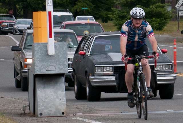 Cyclist crossed a railroad track with a long line of cars behind them.