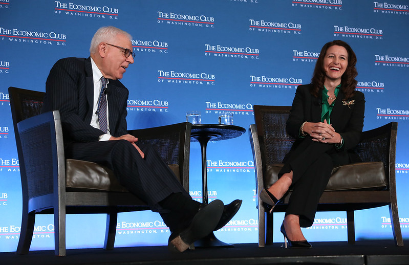 Man and woman sit on a stage, talking and laughing.