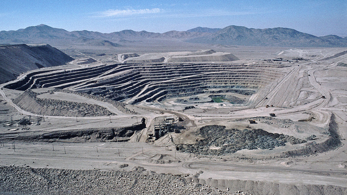 Huge, open-pit mine in the desert, with mountains in the background.