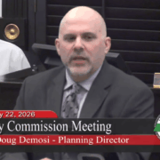 Demosi speaks at a podium on TV.