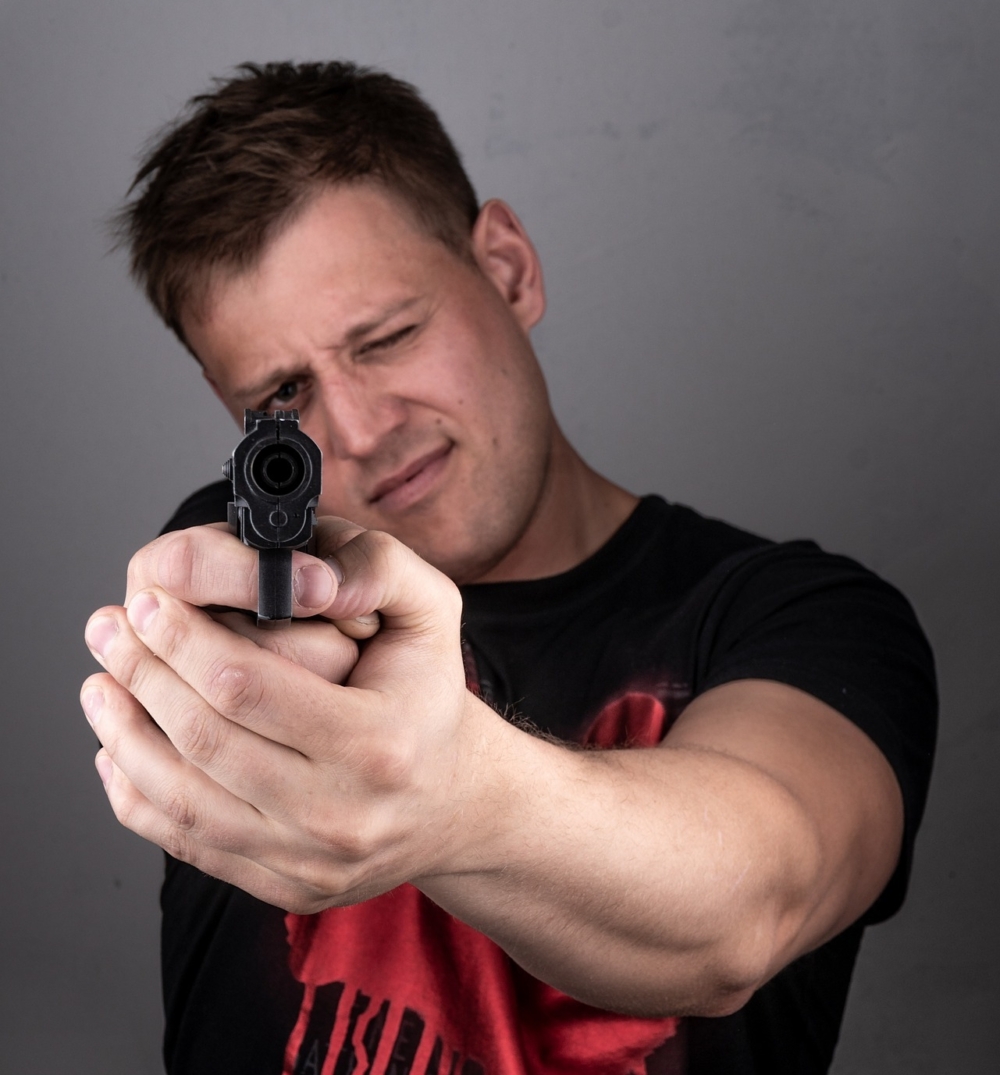 White man with gun pointed at the camera.