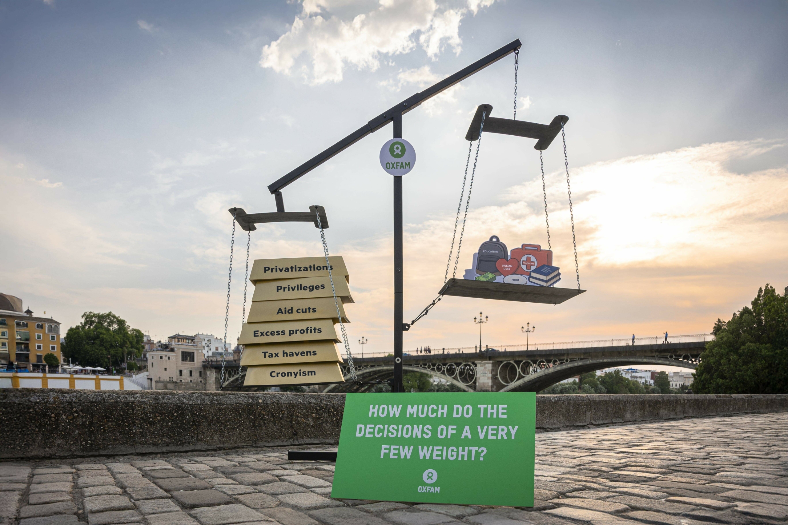 giant scale on the street, with a stack of gold bars outweighing symbols representing social goods