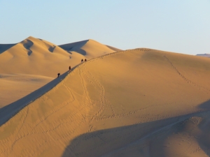 image of sand dunes, with a few tiny individuals walking on one
