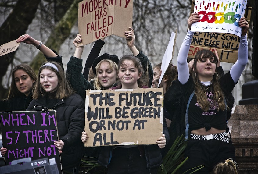 A group of young people hold sings with environmental messaging.