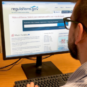 A person sits at a computer with the Regulations.gov homepage up on the screen.