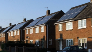 a row of four brown houses, each with solar panels on the roofs