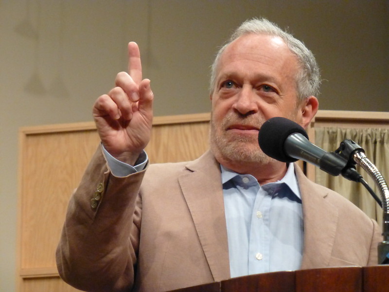 Robert Reich holding a finger up at a podium.