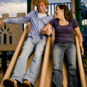 Two adults happily sliding down a double playground slide.
