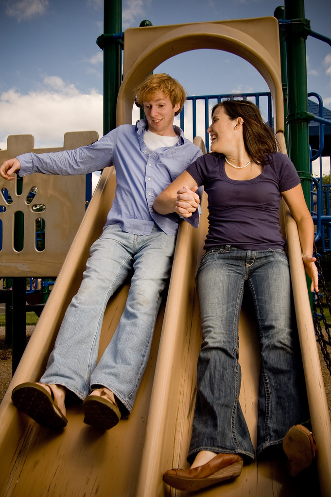Two adults happily sliding down a double playground slide.