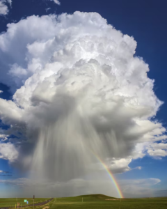 Huge storm cloud against a blue sky, a rainbow, and open, green land.