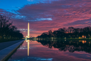 image of the Reflecting Pool in Washington, DC, with the Washington monument in the background and a purple-orange sky that could signal a sunrise or a sunset.