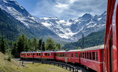 red train rounds a bend with white-peaked mountains in the background