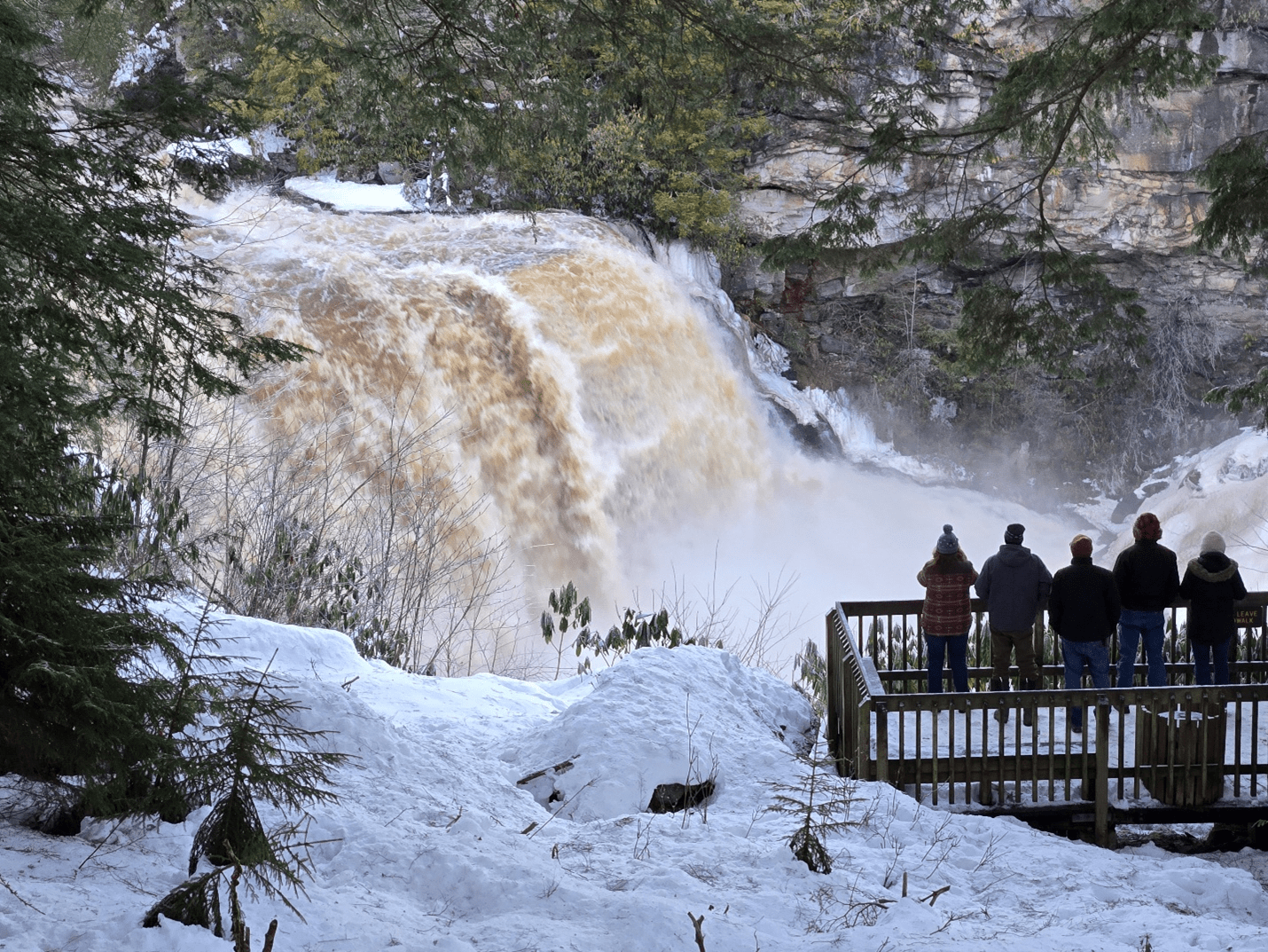 The 62-foot high waterfall at Blackwater Falls State Park on a frozen winter day. Tourists on a wooden overlook are dwarfed by the size of the waterfall. 