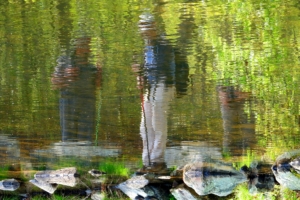 reflection of two hikers looking at a pond
