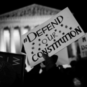 Protest sign that reads "Defend Our Constitution" held up in a crowd outside the U.S. Supreme Court